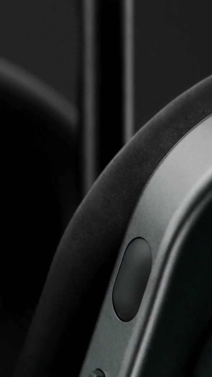 Gros plan sur le coussinet et le bouton ovale d’un écouteur du casque Nothing, dans une lumière sombre.